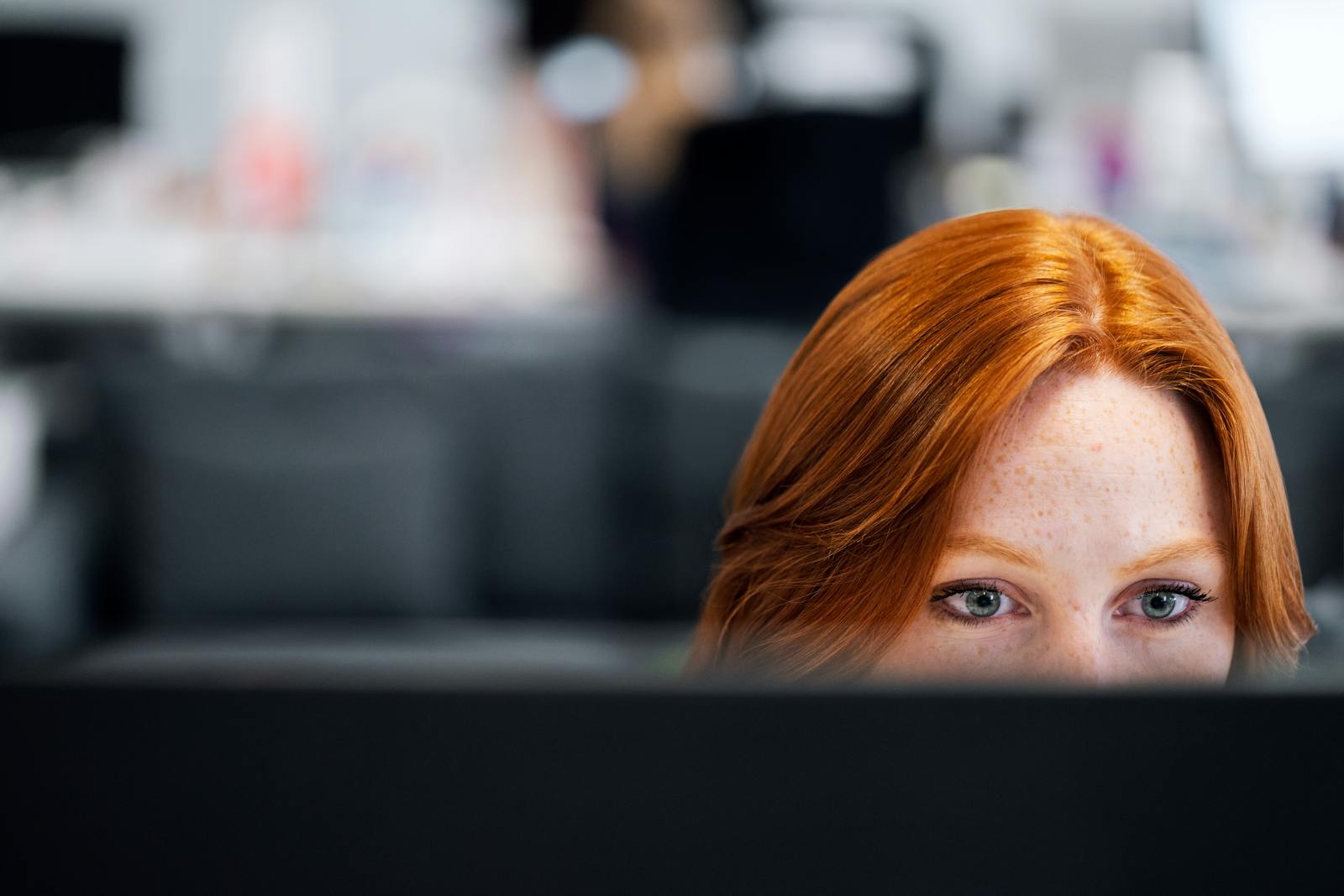 A woman with red hair intensely focused on a computer screen in an office setting.