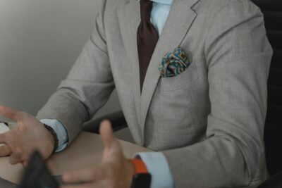 Close-up of a businessman gesturing during a meeting, wearing a stylish gray suit and pocket square.