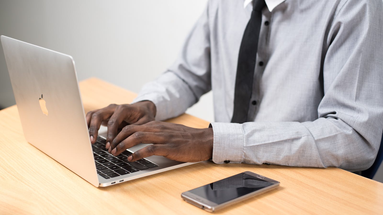Businessman typing on a laptop in a modern office setting with a smartphone on the desk.