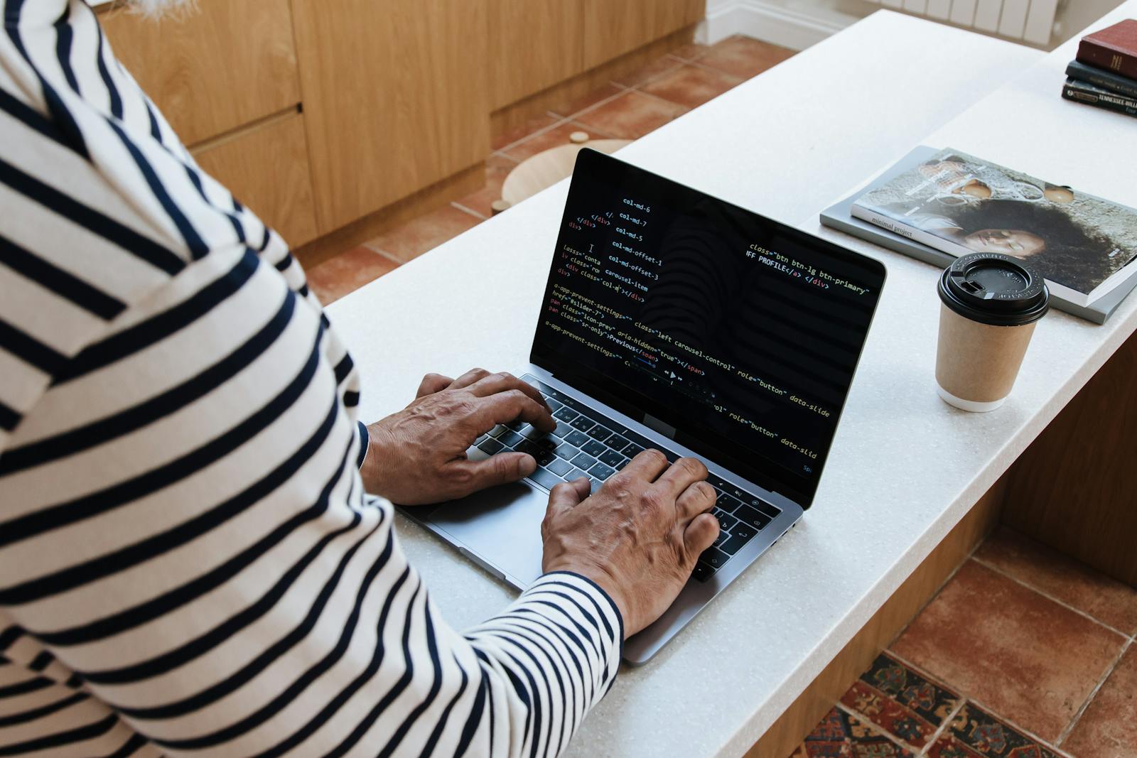 A senior adult programmer coding at home on a laptop, showcasing a work-from-home setup.