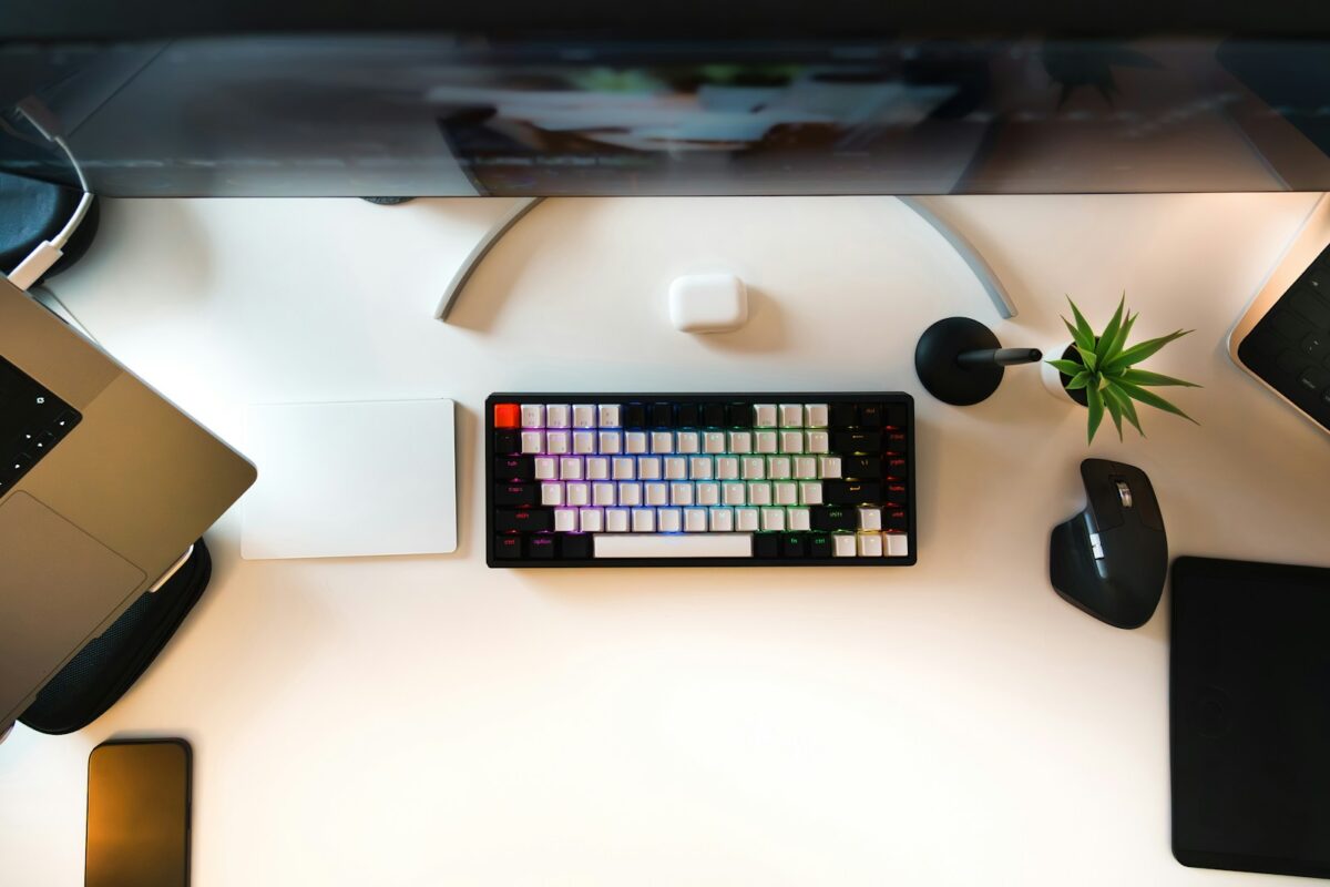 A desk with a laptop, keyboard, mouse and a plant