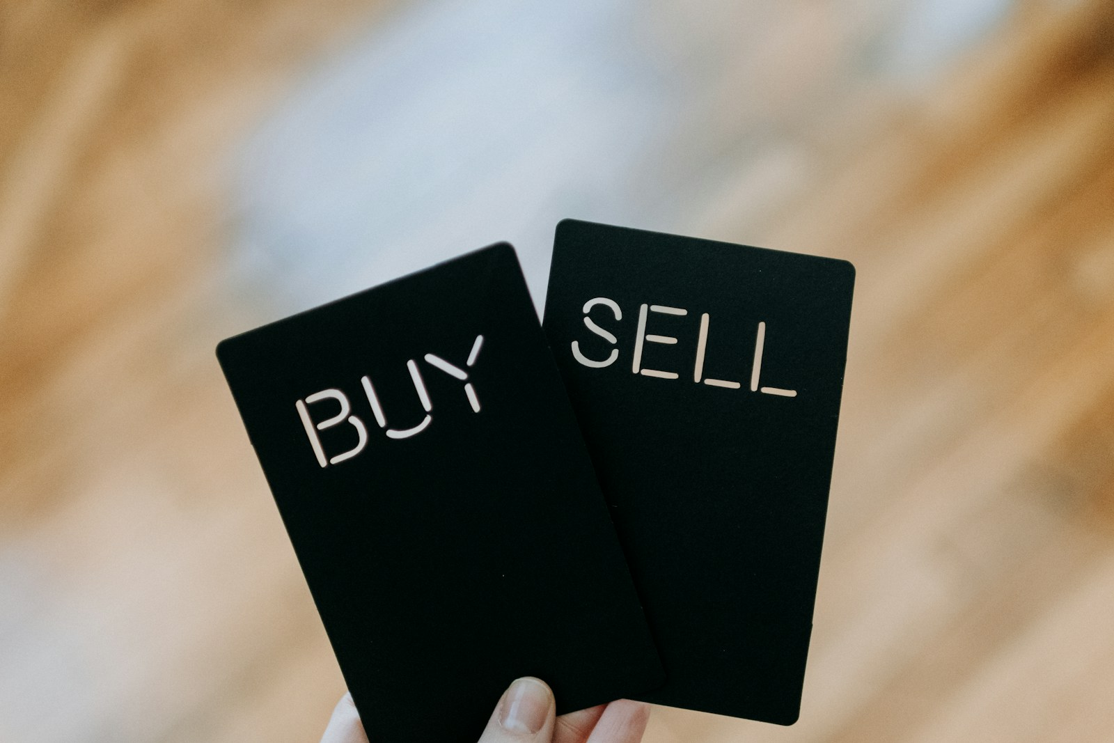 A hand holding two black cards labeled ‘BUY’ and ‘SELL,’ representing decision-making and sales strategies within Sales Playbooks in CPQ.