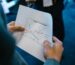 Close-up of hands holding a paper with a line graph showing product trends by month during a business meeting.