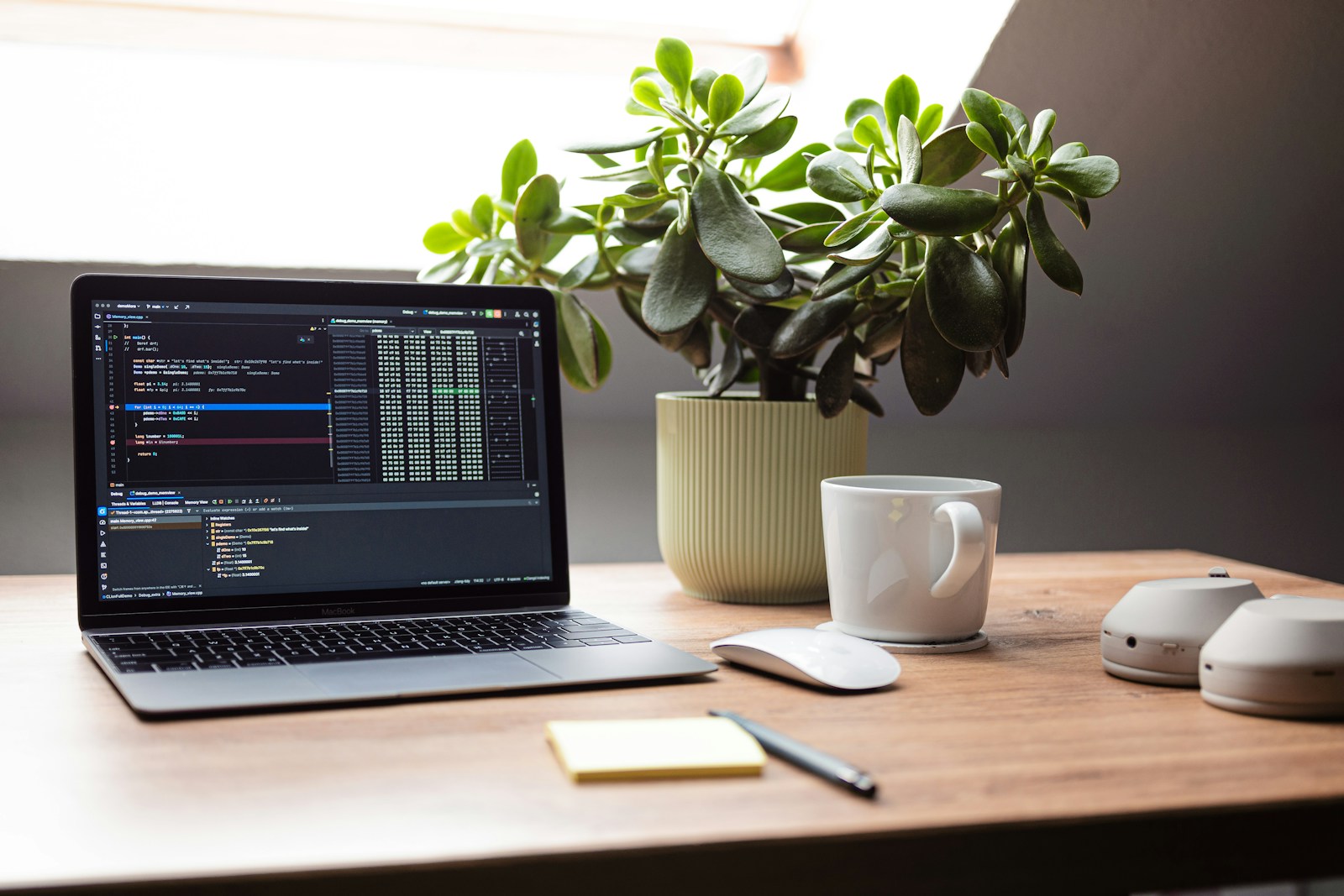 Laptop with code, plant, and mug on desk.