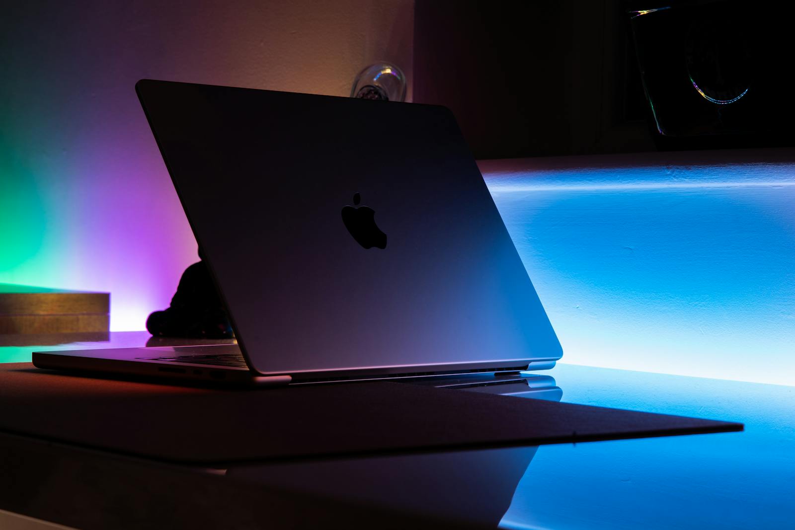A MacBook reflecting vibrant neon lights in a dimly lit room setting.