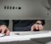 A focused close-up of hands typing on a sleek, modern computer setup in an office environment.