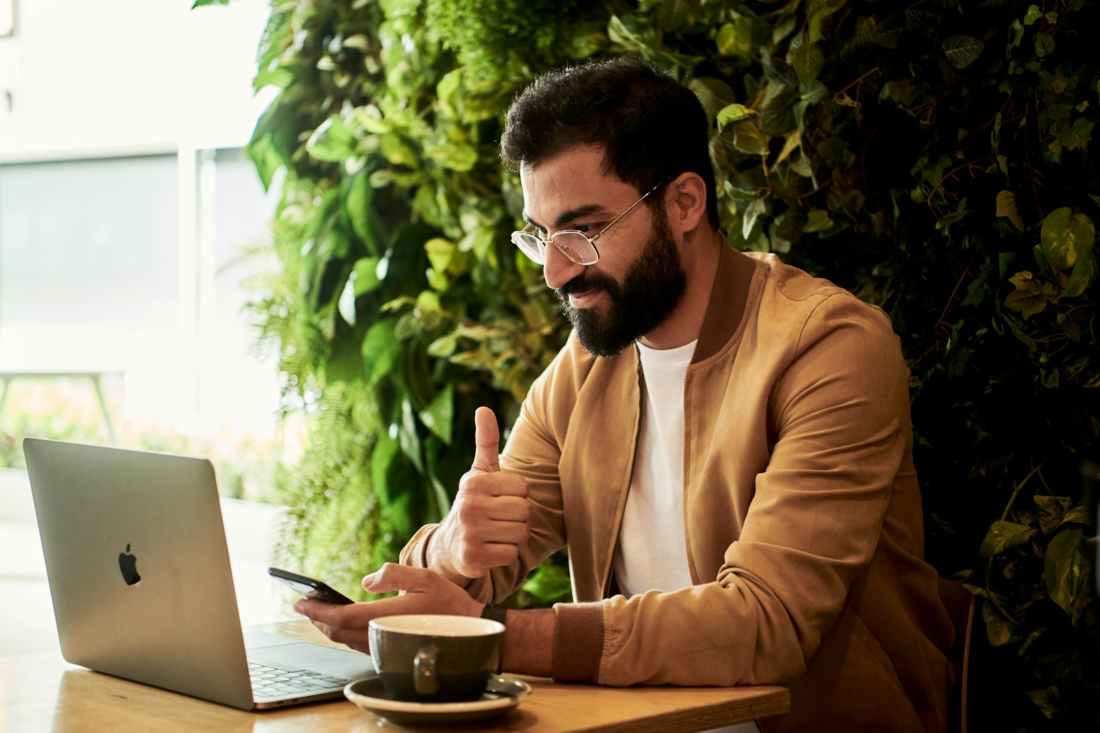 Professional working on a laptop and smartphone in a modern workspace, giving a thumbs up, representing efficient SAP CPQ support and seamless customer assistance.