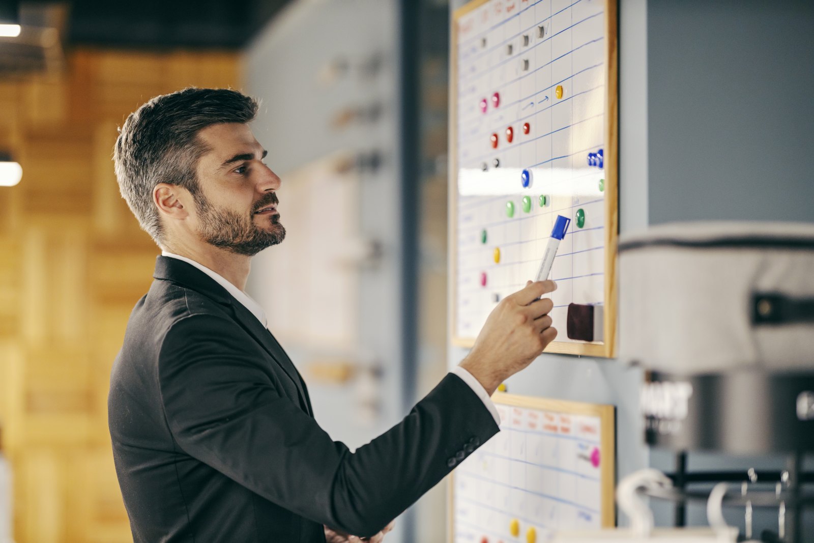 A man in a suit moving a coloured magnet on a large wall planning board in an office