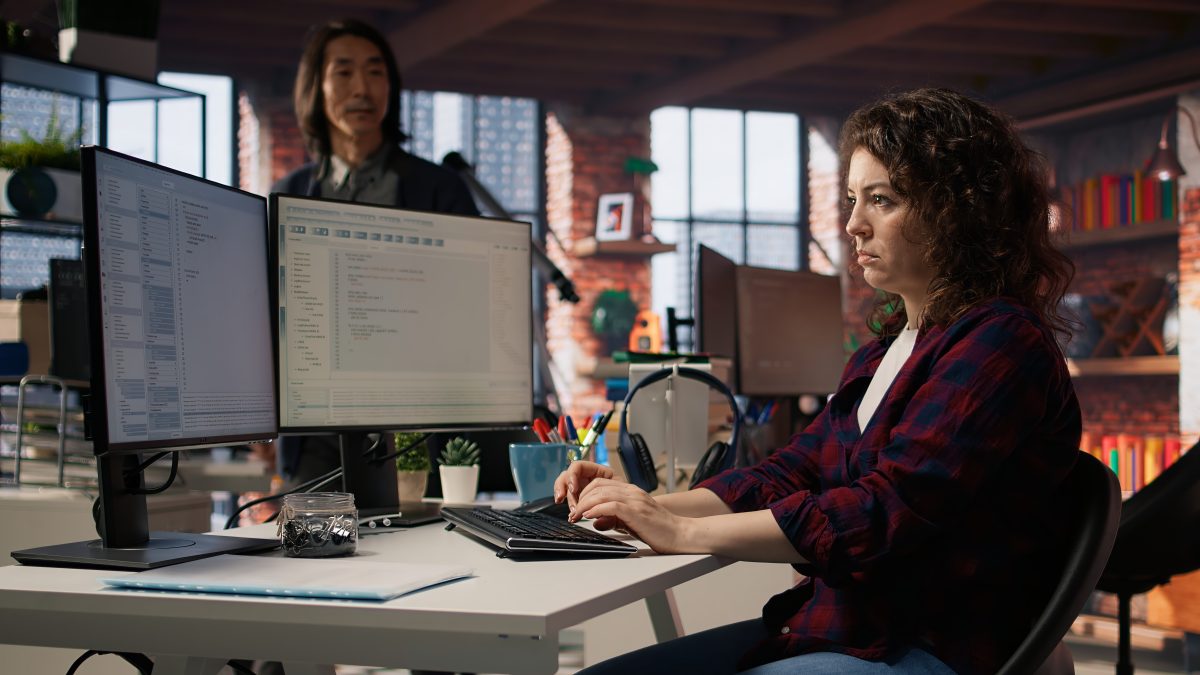 Software developer reviewing code on two monitors in an office