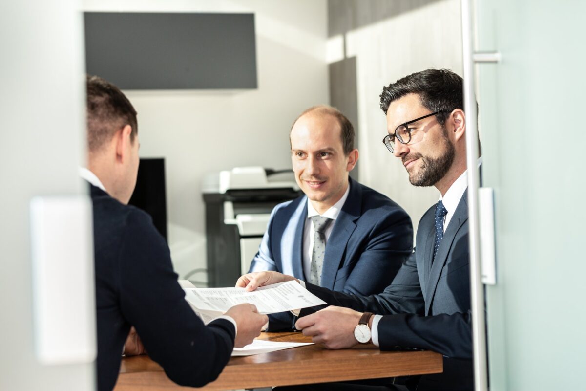 Business team reviewing and signing a contract at an office table, representing an approval being reviewed before it moves forward