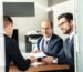 Business team reviewing and signing a contract at an office table, representing an approval being reviewed before it moves forward