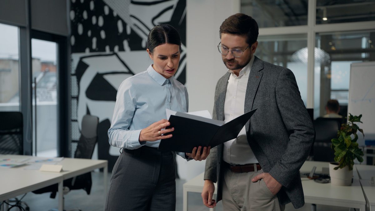 Two colleagues in an office reviewing paperwork in a folder together, discussing a document that needs a decision